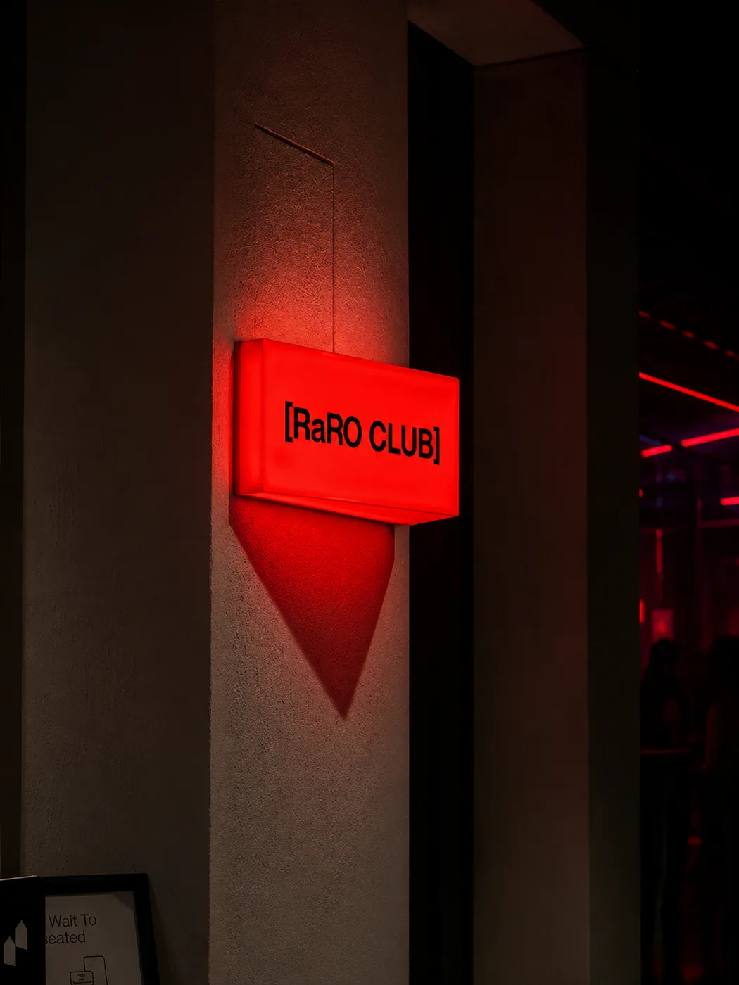 Letreiro luminoso vermelho escrito Raro Club em um corredor escuro